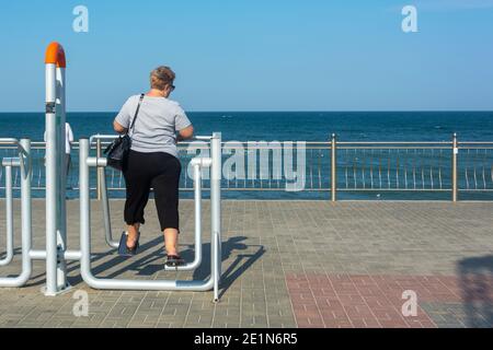 Overweight woman goes in for sports on public simulator by sea. Overweight concept, warm-up. Stock Photo