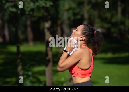 Side portrait of tired young woman wiping her sweat on her neck after fitness exercises outdoor Stock Photo