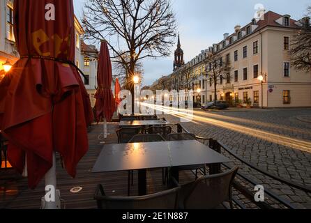 Dresden, Germany. 08th Jan, 2021. Empty tables and closed umbrellas are standing in front of a restaurant while on the Königstraße the headlights of passing cars draw light trails. (Shot with long exposure time) Credit: Robert Michael/dpa-Zentralbild/dpa/Alamy Live News Stock Photo