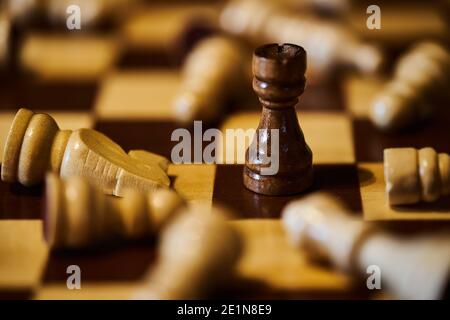 Black rook stands upright on chessboard, surrounded by fallen white pieces Stock Photo