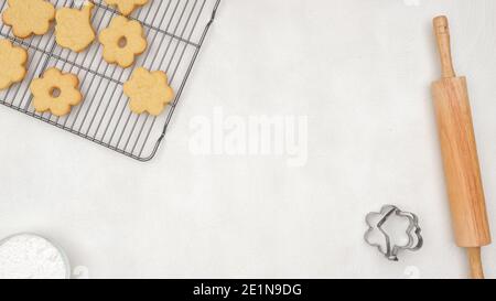 Food background. Fresh baked cookies on cooling rack, wooden rolling, cookie cutters, flat lay with copy space Stock Photo