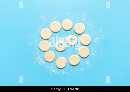 Making donuts scene with raw yeast dough cut in round shape for ring doughnuts, isolated on blue background. Homemade uncooked dough. Baking flat lay. Stock Photo