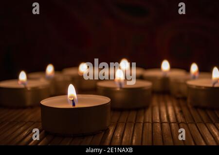 Burning candles on a wooden table, close up. Nine tea lights on bamboo mat, selective focus with copy space Stock Photo