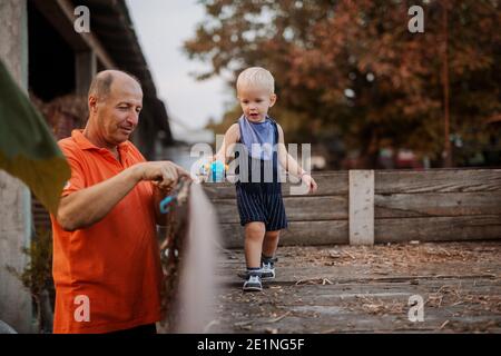 Boys and cars. Grandfather and grandson playing with car toys in the farm backyard. Cute baby boy standing in a wooden trailer. Stock Photo