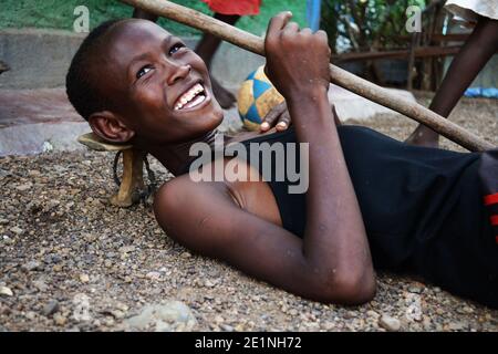 Portrait of a Kenyan teenage boy from Turkana tribe posing with a stick and a head stand used by local pastoralists. Taken in Kakuma town in Kenya. Stock Photo