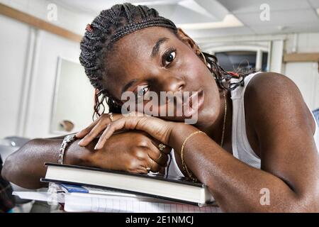 Closeup portrait of bored young African American student resting on stack of books in classroom Stock Photo