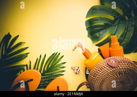 Sunscreen bottles arranged in straw bag on a bright yellow background with palm leaves, top view Stock Photo