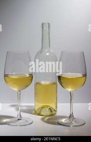 Transparent bottle with white wine inside and two glasses with white wine on a white background. Stock Photo
