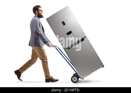 Full length profile shot of a bearded man walking and pushing a hand truck with a refrigerator isolated on white background Stock Photo