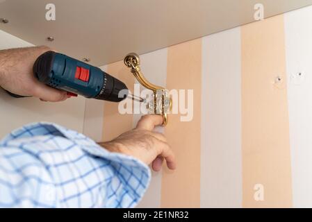 Man using a professional screwdriver while installing a decorative wardrobe hook Stock Photo
