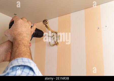 Man using a power screwdriver while installing a decorative wardrobe hook Stock Photo