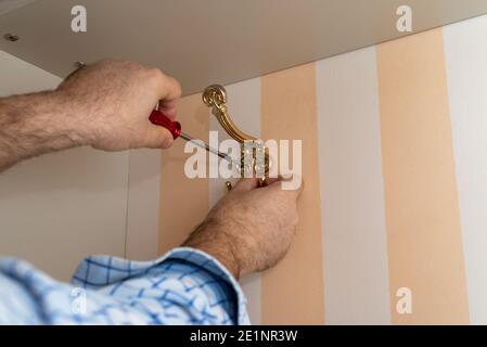 Man using a screwdriver while installing a decorative wardrobe hook Stock Photo