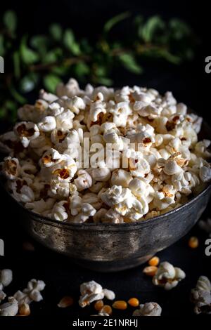 Prepared popcorn in frying pan, corn seeds in bowl and corncobs on dark background. Stock Photo