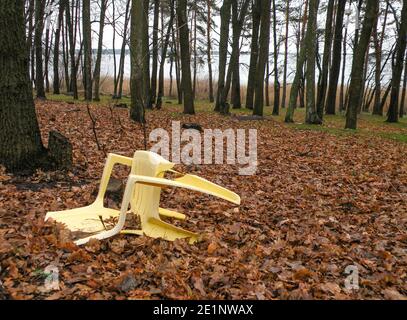 Environmental concerns from pollution of the forest and other natural environment. Plastic chair thrown in the forest by the lake and other plastics t Stock Photo