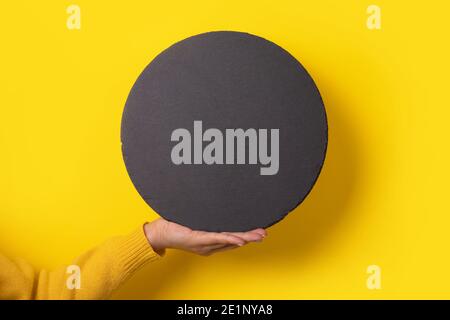 round black slate board on hand over yellow background,  empty space for menu or recipe. Stock Photo