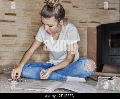 Close up of a caucasian girl picking a wooden pin or metallic screw from a group with several screws, nuts, bolts, rivets, nails and washers on the fl Stock Photo