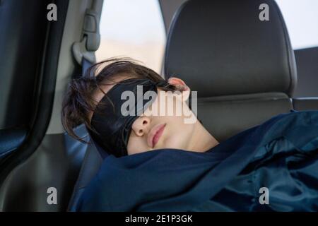A child sleeps in a car seat wearing an eye mask covered in a blanket Stock Photo