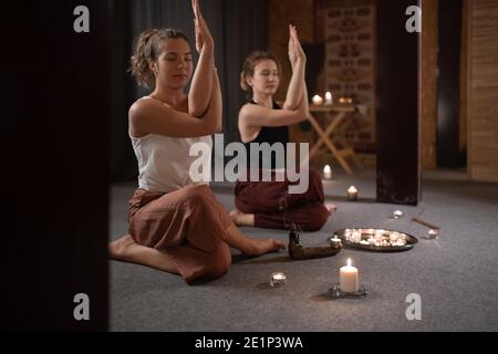 Young women meditating in Knee Pile pose with eagle arms while doing yoga together Stock Photo