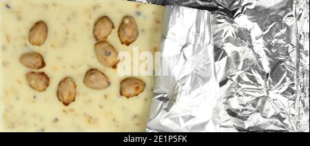 White chocolate pieces with pistachios and almonds isolated on white background. White chocolate bar in opened foil wrapping Stock Photo