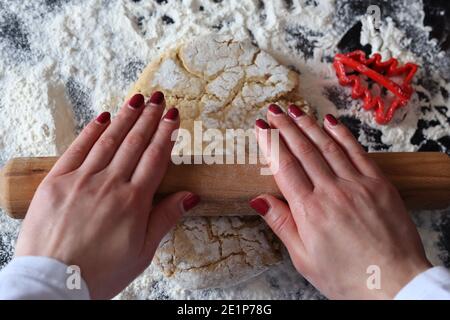 Woman hands with a rolling pin roll out the cookie dough on the kitchen table. Homemade prepare and decoration food concept Stock Photo