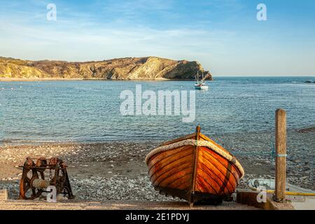 LULWORTH, DORSET, UK - MARCH 17, 2009:  Traditional wooden rowing boat pulled  up on beach next to old rusty beach winch Stock Photo