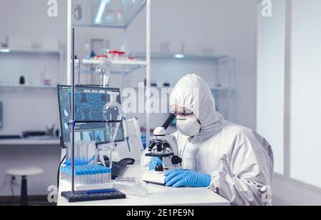 Microbiologist conducting experiments in modern laboratory with microscppe. Virolog in coverall during coronavirus outbreak conducting healthcare scientific analysis. Stock Photo