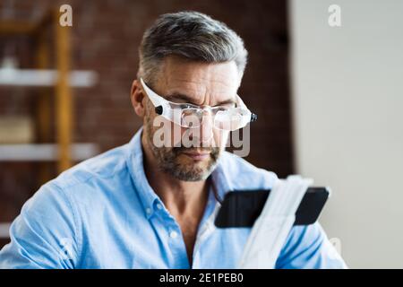 Mature Man Using Magnifying Glasses For Reading Text On Smartphone Stock Photo