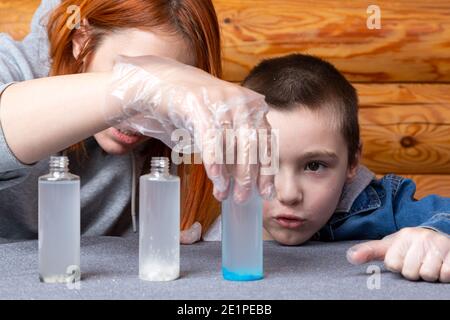 Close-up of a woman in disposable gloves pours a chemical element from a test tube into a bottle on the table, and the boy attentively observes the ex Stock Photo