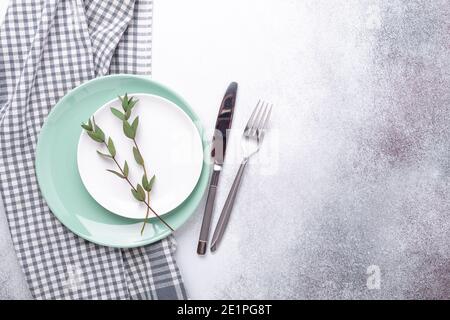 Empty mint and white plates, linen napkin, eucalyptus leaves and cutlery on stone background Copy space Top view - Image Stock Photo