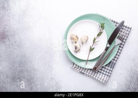 Easter table setting. Empty mint and white plates, linen napkin, eucalyptus leaves and eggs on stone background - Image Stock Photo