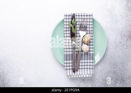 Easter table setting. Empty mint and white plates, linen napkin, eucalyptus leaves and quail eggs on stone background - Image Stock Photo