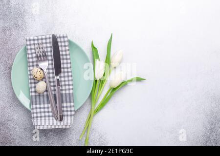 Easter table setting. Empty mint and white plates, linen napkin, white tulips and quail eggs on stone background - Image Stock Photo