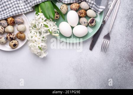 Beautiful Easter composition. Green mint plate, easter eggs, hyacinth and silver cutlery on stone background. Copy space. Top view - Image Stock Photo