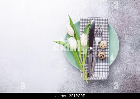 Easter table setting. Empty mint and white plates, linen napkin, white tulips and quail eggs on stone background - Image Stock Photo