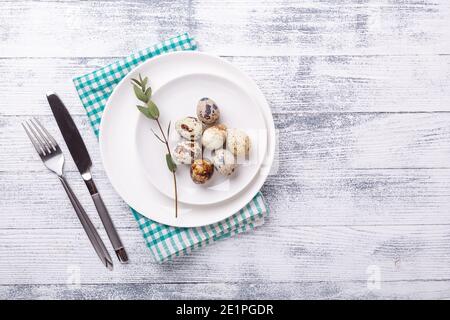 White plate with quail eggs and cutlery on wooden background. Easter composition. Copy space. Top view - Image Stock Photo