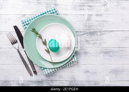 White and green mint plate with Easter eggs and cutlery on wooden background. Easter composition. Copy space. Top view - Image Stock Photo