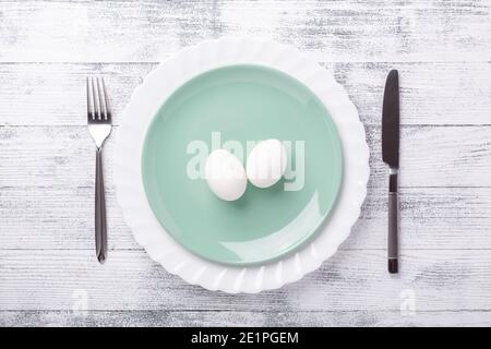 Spring table setting. Green mint plate, Easter eggs and cutlery on wooden background. Easter composition. Copy space. Top view - Image Stock Photo