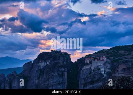 Twilight over Varlaam and Great Meteoron monasteries in Meteora, Greece. Underexposed, great sunset with clouds and sun rays. UNESCO World Heritage Stock Photo