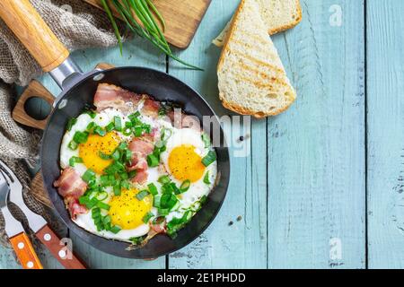 Spring scrambled eggs with green onions and bacon in a cast iron skillet on a rustic wooden background. Top view flat lay. Copy space. Stock Photo