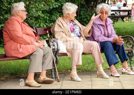Three elderly women are sitting on a bench in a city park. Seniors talking, Old women bench, old people talking, population friends outdoors Stock Photo