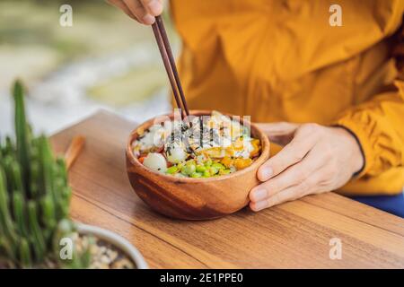 Man eating Raw Organic Poke Bowl with Rice and Veggies close-up on the table. Top view from above horizontal Stock Photo