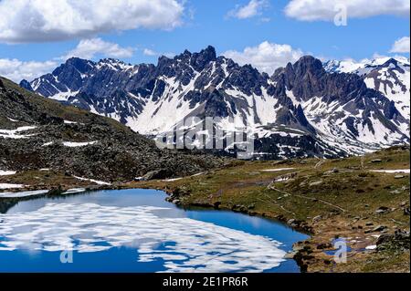 High-altitude lake still covered with ice. In the background a grey mountain range and a beautiful blue sky. Stock Photo