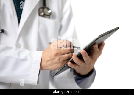 A standing male doctor in long white hospital gown writing on a tablet. Isolated on white background. Stock Photo