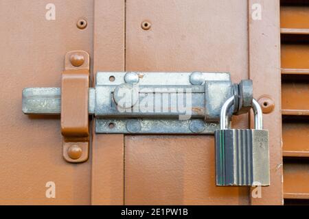 A close up of a metal slide lock and a padlock on the exterior of a door Stock Photo