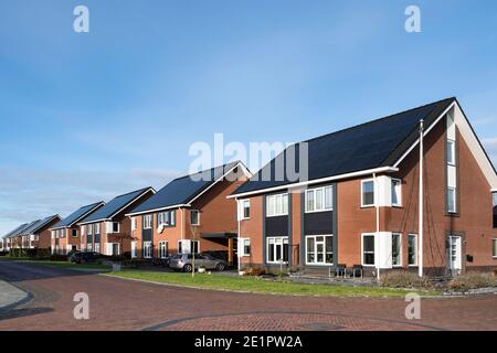 Solar panels mounted on the roofs of a row modern new-build houses in a street Lemmer, Friesland, the Netherlands with blue sky Stock Photo