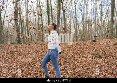 Happy adult girl enjoying in forest with autumn leaves falling in amazing landscape.Copy space Stock Photo