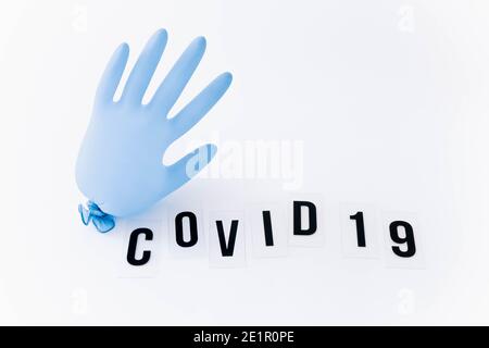 Coronavirus or covid-19 concept with a protective glove in shape of balloon. Covid 19 in letters on white table Stock Photo