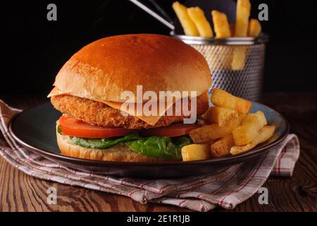 Chicken fillet in a in a brioche bun with lettuce tomatoes and cheese and skin on fries shot with creative lighting Stock Photo