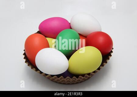 Multi colored painted easter eggs in red, pink, yellow, green and white in a brown paper basket against a white background. Stock Photo