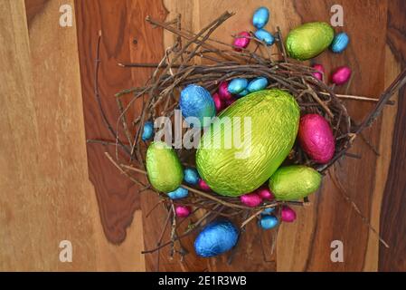Foil wrapped colourful easter eggs in pink, green, blue and yelow in a natural nest made of sticks and twigs. There is one large egg in the middle. Stock Photo